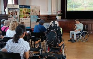 Eine Tagung im KEH mit Teilnehmern in Rollstühlen, die einem Vortragenden zuhören.