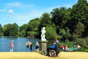 Menschen genießen einen sonnigen Tag am See im Schlosspark Charlottenburg in Potsdam. Eine Statue steht im Vordergrund, während andere die Natur bewundern.