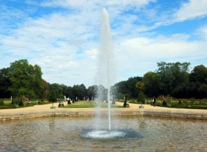 Ein hoher Wasserstrahl im Schlossgarten Charlottenburg, umgeben von grünen Bäumen und gepflegten Hecken.