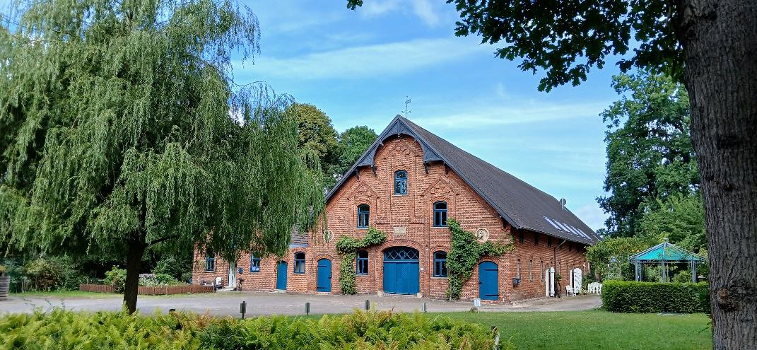 Ein malerisches Backsteingebäude mit blauen Türen und Fenstern, umgeben von üppiger Vegetation und Bäumen.