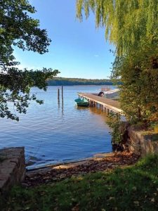 Ein ruhiger See mit einem Steg und einem kleinen Boot, umgeben von grünen Bäumen und klarer Luft.