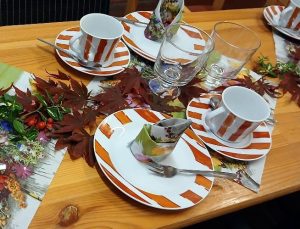 Eine festlich gedeckte Tisch mit herbstlichen Elementen, Porzellantellern und Gläsern.