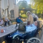 Menschen mit Locked-in-Syndrom und Unterstützer tauschen sich im Zenner Biergarten aus. Sie nutzen Kommunikationshilfen und genießen die Gemeinschaft.