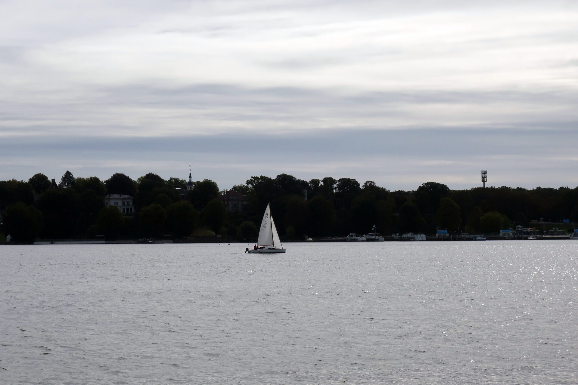 Blick vom Garten über den Wannsee auf ein Segelboot vor bewaldetem Ufer